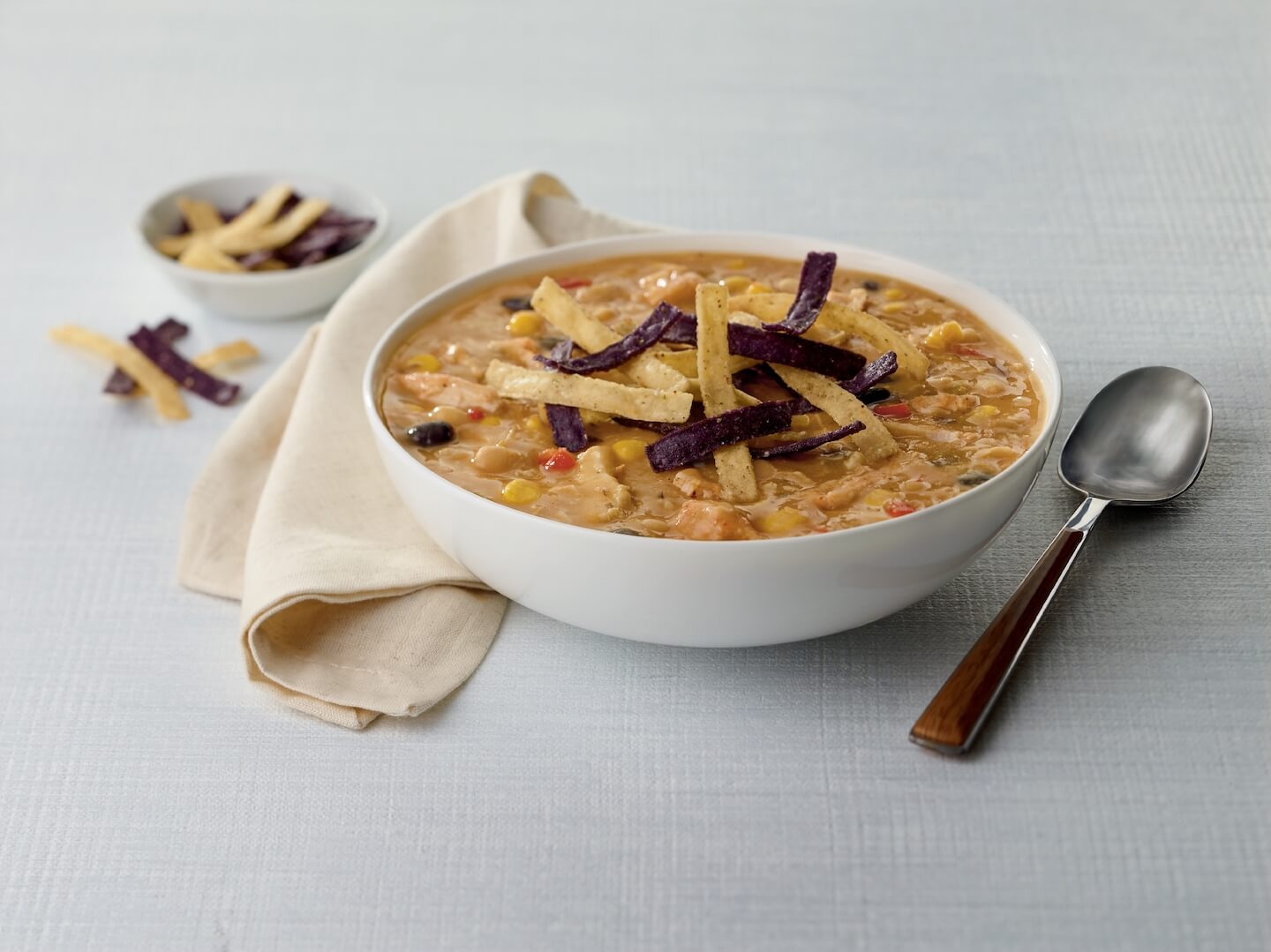 Bowl of Chick-fil-A Chicken Tortilla Soup surrounded by beans, corn, celery and a spoon.