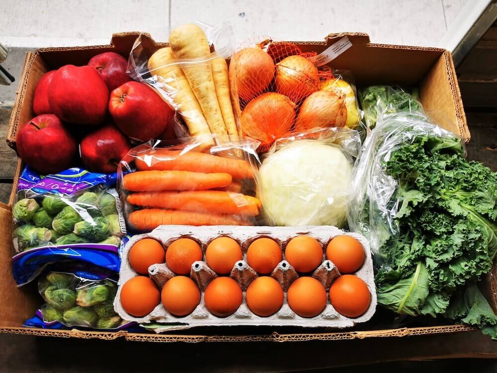 a box of fresh produce including eggs, carrots, apples and vegetables