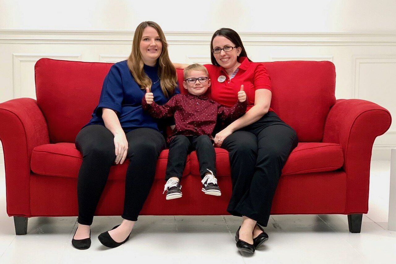 Two women sitting on either side of a young boy on a red couch