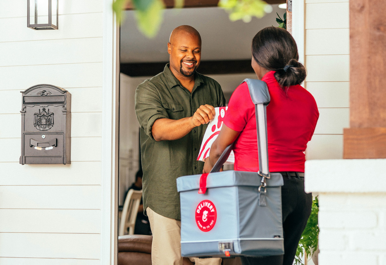 A Team Member with a Chick-fil-A Delivery bag hands a customer his order at the door of his home. 