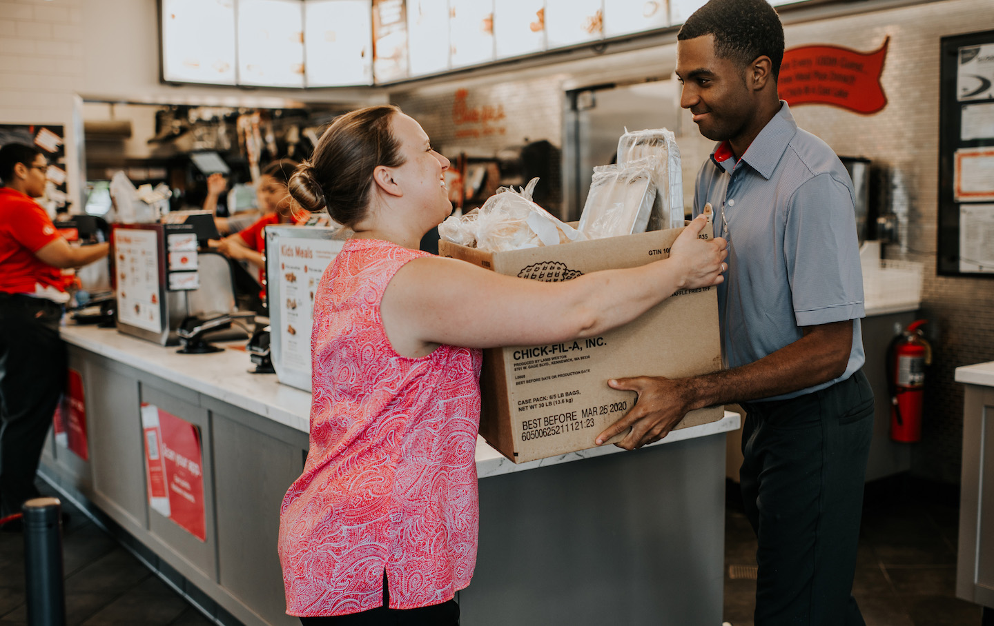 A Chick-fil-A Team Member hands a representative from a local nonprofit a box of surplus food from the restaurant through the Chick-fil-A Shared Table program. 