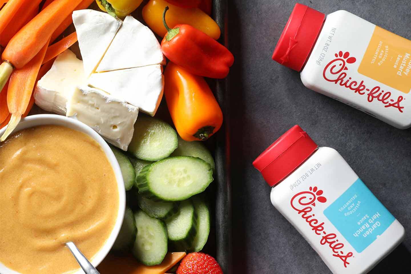 Platter of veggies and cheese with bowl of Honey Mustard Sauce and two Chick-fil-A bottled sauces laying on their side