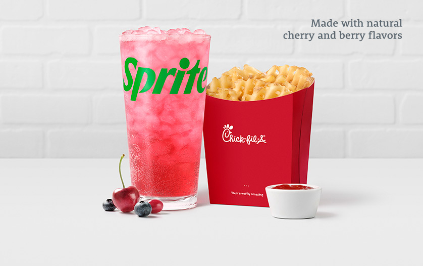 A glass of Cherry Berry & Sprite® with cherries and berries sitting in front of it, sitting next to Waffle Fries