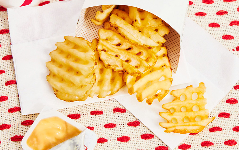 Waffle Fries in a carton on white napkins and a red and white tablecloth