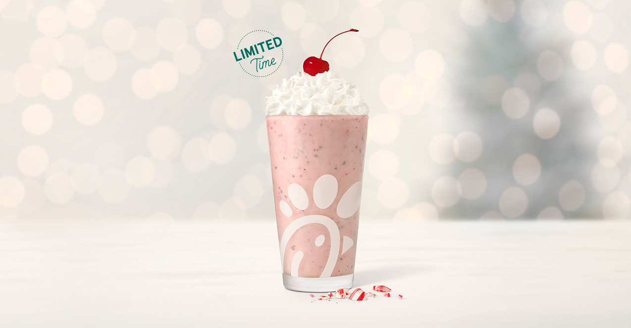 Glass of a Peppermint Chip Milkshake, sitting next to pieces of peppermint, with twinkling holiday lights in the background with green text that says "Limited Time"