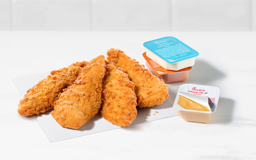 4-count Chick-fil-A Chick-n-Strips® next to packets of Garden Herb Ranch Sauce, Zesty Buffalo Sauce and Chick-fil-A® Sauce on a white countertop with a white tiled background