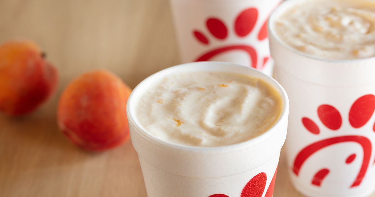 Cups of Peach Milkshake on a table with peaches next to them 