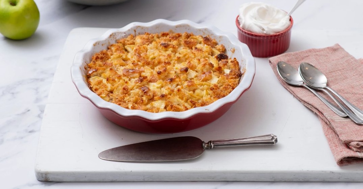 Apple Cobbler in a pie pan on a white tray with a napkin and serving utensils around it 