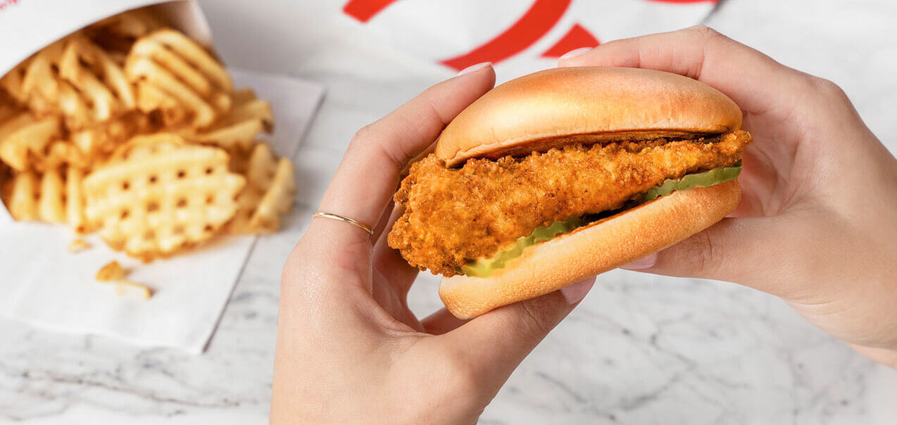 Hands holding the original Chick-fil-A Chicken Sandwich next to a side of waffle fries.