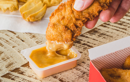 A person dipping a Chick-fil-A Chick-n-Strip® into Chick-fil-A® Sauce with Waffle Fries in the background