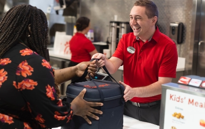 Chick-fil-A team member handing a catering bag filled with food to a customer.