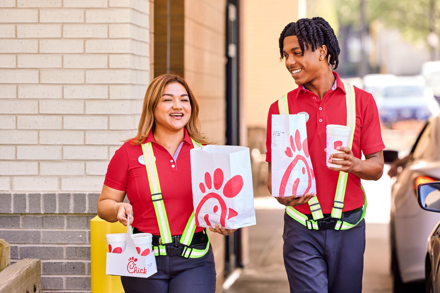 Two Chick-fil-A employees delivering orders to customers in the drive-thru. 