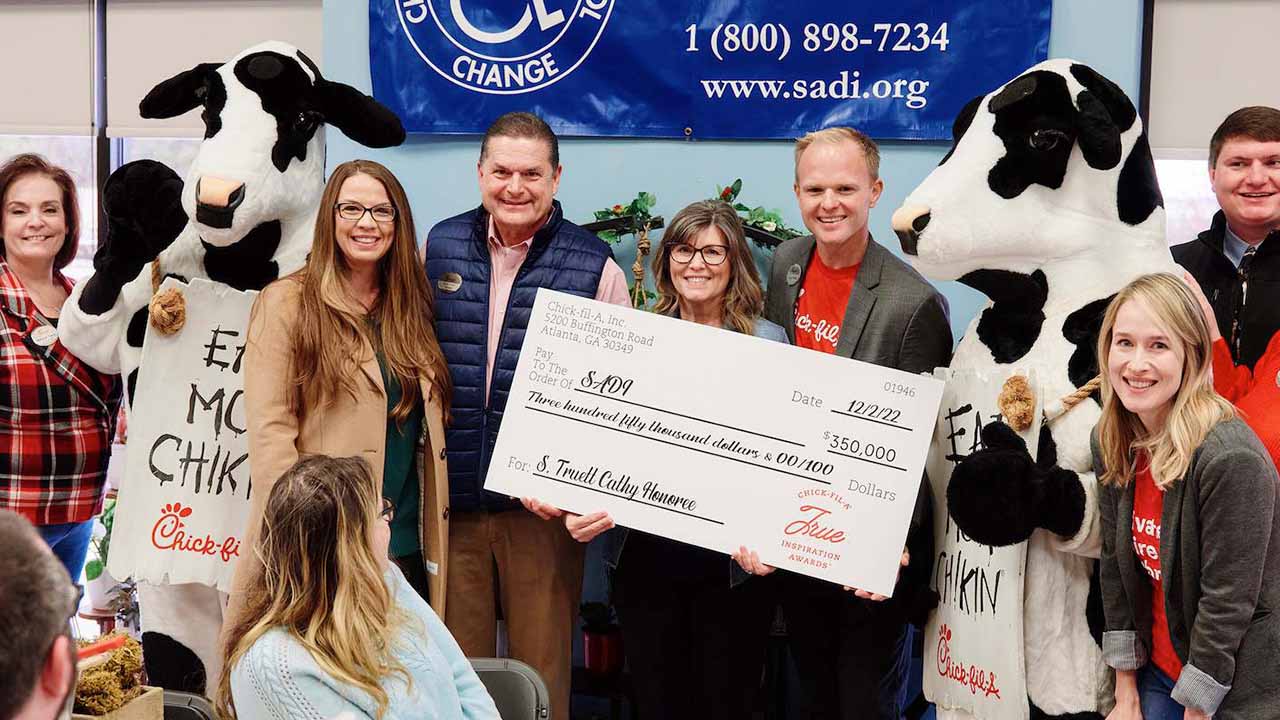 A Chick-fil-A Team Member receiving a True Inspiration Scholarship while being cheered on by her Teammates and S. Truett Cathy Brands (STC) leader John White IV.