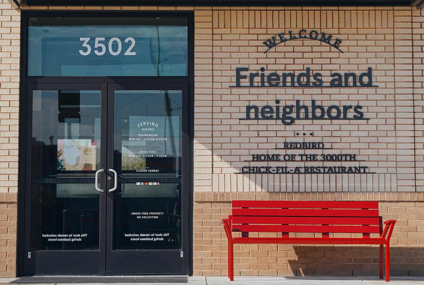 The exterior of Chick-fil-A RedBird featuring a red bench and writing on the restaurant wall that reads, "Welcome friends and neighbors. RedBird Home of the 3000th Chick-fil-A Restaurant".