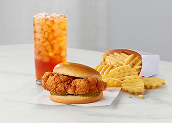 The Chick-fil-A Cauliflower Sandwich alongside a serving of Chick-fil-A Waffle Fries and an iced tea on a white countertop.