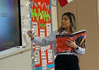 Former Chick-fil-A Team Member Carolina Olivares standing at the head of a classroom while holding a textbook and lecturing her fifth-grade students in Laredo, Texas.
