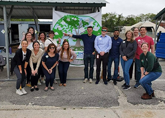 Chick-fil-A staff posing in front of a climate change challenge banner in an outdoor gazebo area.