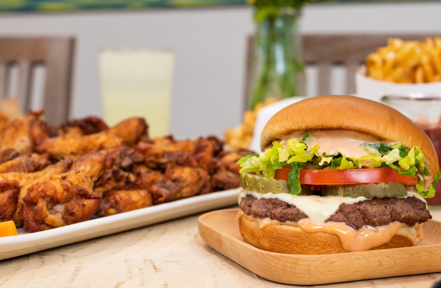 A burger topped with cheese, lettuce, tomato and burger sauce next to a plate of chicken wings and fries from Little Blue Menu.