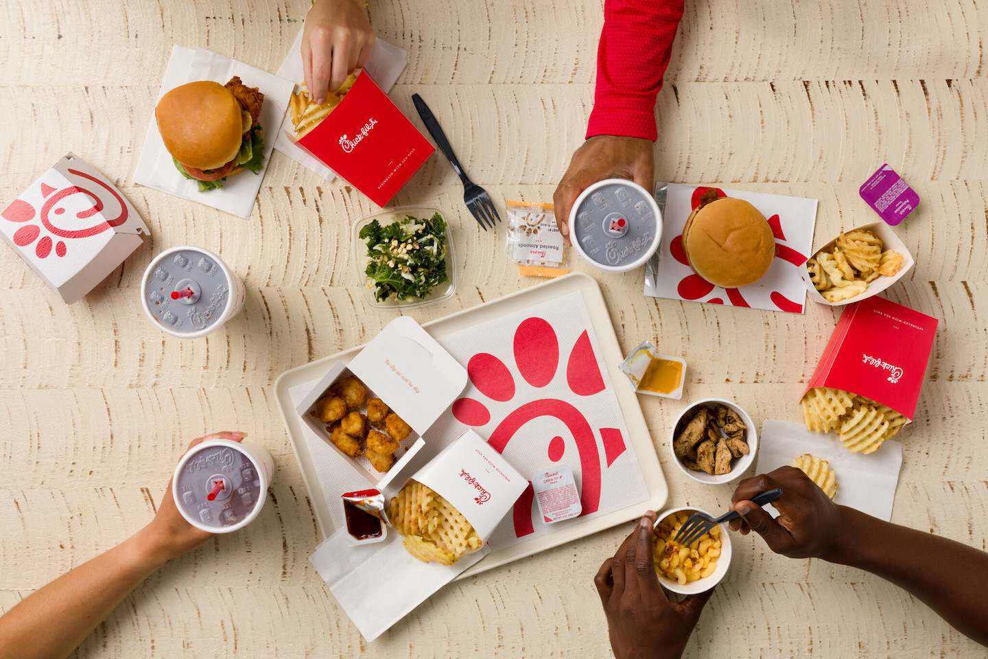 Chick-fil-A sandwiches, nuggets, sides, sauces and drinks on a white table with a white tray in the center.