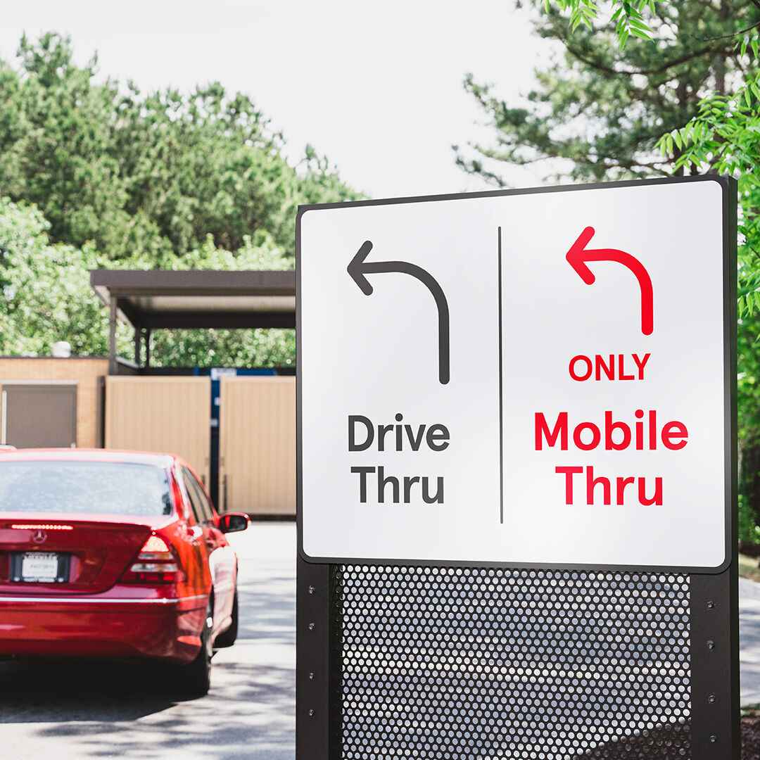 A mobile thru sign in a Chick-fil-A restaurant drive-thru with black text reading "Drive Thru" and red text reading "Only Mobile Thru" and a red car in the lane. 