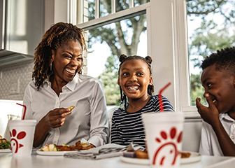 A family smiling and enjoying different Chick-fil-A meals at their kitchen table.