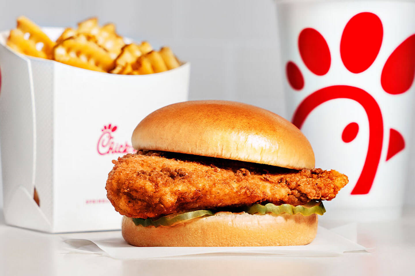 A Chick-fil-A Chicken Sandwich sits in front of a carton of Waffle Potato Fries and a drink. 