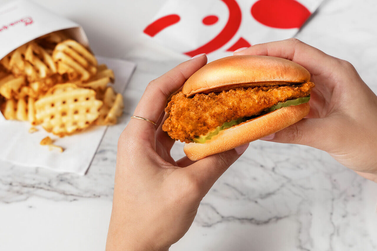 Closeup of a person's hands holding the Chick-fil-A® Chicken Sandwich with Waffle Potato Fries™ in the background.