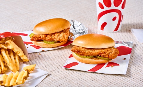 Two Chick-fil-A sandwiches on their wrappers next to an order of Waffle Potato Fries and a Chick-fil-A drink.