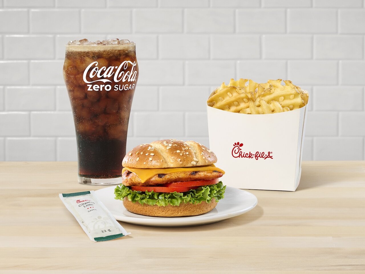 Grilled Spicy Deluxe Sandwich sitting on a white plate with Waffle Fries and a Coca Cola glass in the background.