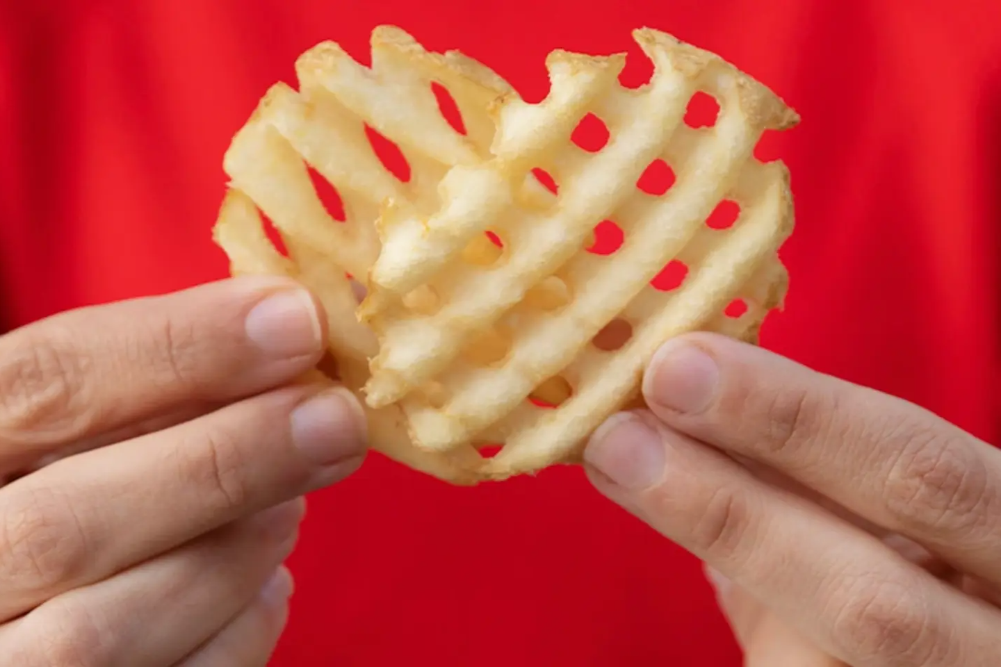 Hands holding a heart-shaped Chick-fil-A Waffle Potato Fry. 