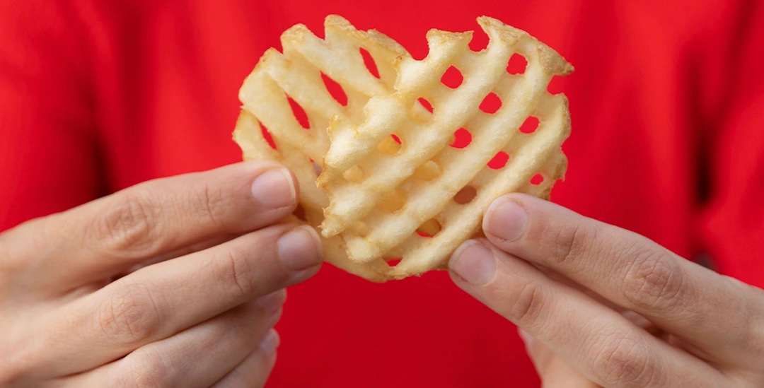 Hands holding a heart-shaped Chick-fil-A Waffle Potato Fry. 