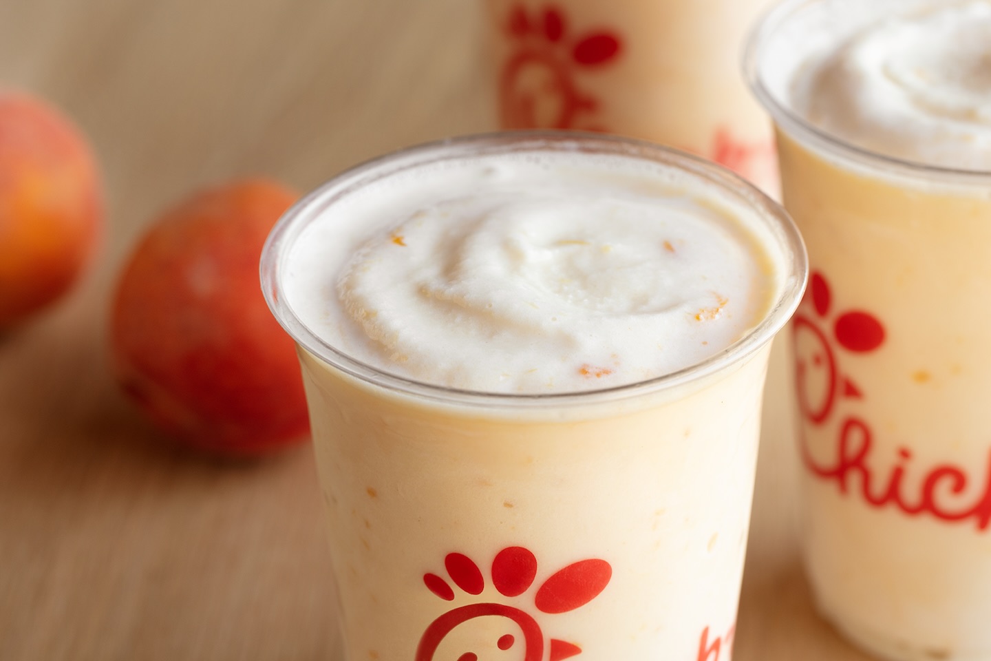 Chick-fil-A Peach Milkshakes sitting on table with peaches in background.