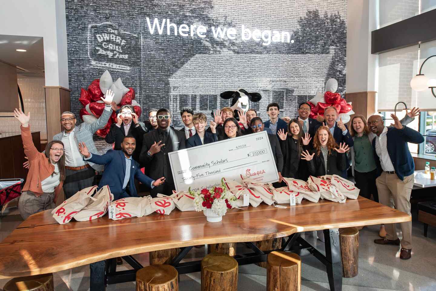 The recipients of the 2024 Chick-fil-A Community Scholarship posing with a large check behind a wall that depicts the Dwarf House and reads "Where we began."