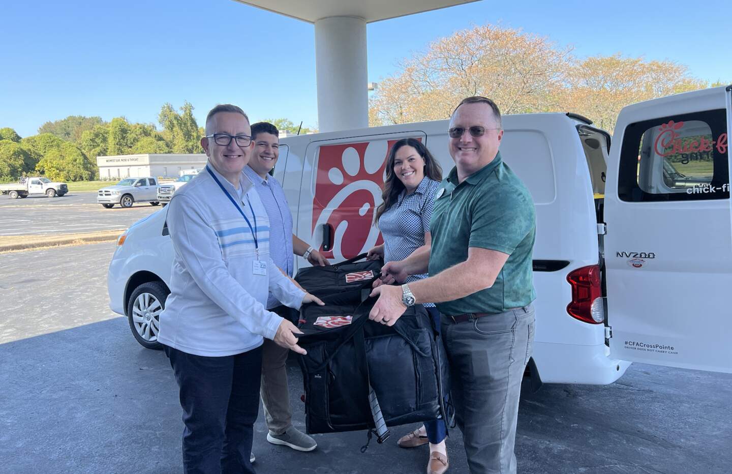 Chick-fil-A Team Members and Evansville Partnership members holding a cooler standing in front of a Chick-fil-A van. 