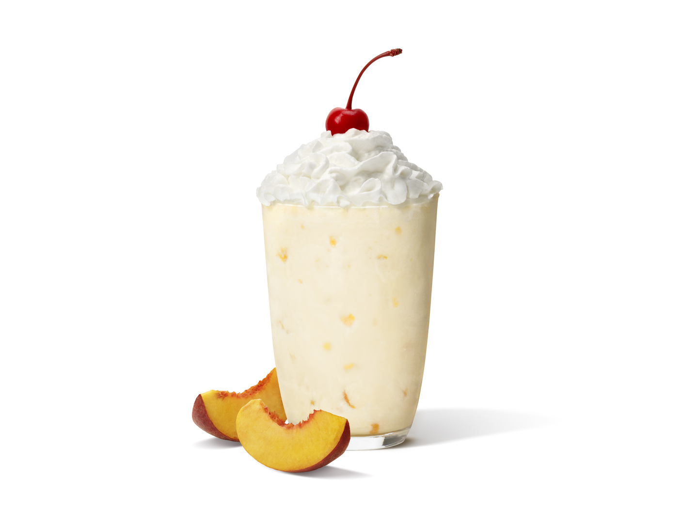 The iconic Chick-fil-A Peach Milkshake next to two slices of peaches on a plain white background.