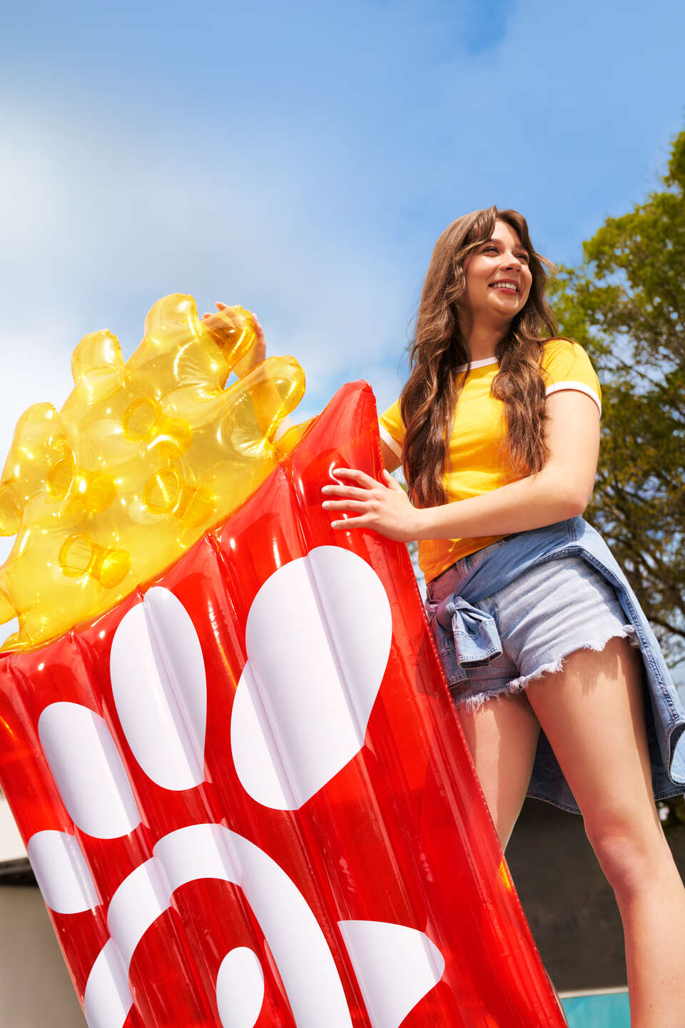 A woman in a yellow shirt and jean shorts holding the Chick-fil-A Waffle Fry Pool Float from the 2024 Summer Merchandise Launch.
