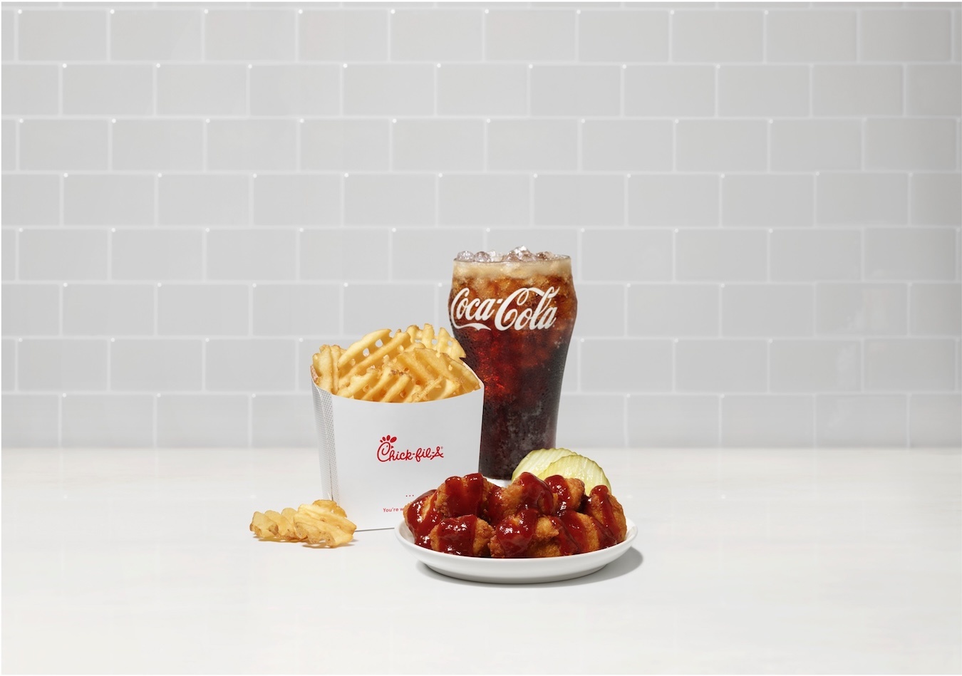 The Chick-fil-A Smokehouse BBQ Nuggets sitting on a plate with Waffle Fries and soda sitting behind.