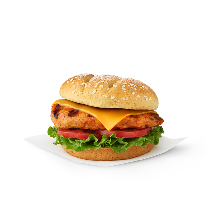 The Grilled spicy Deluxe Sandwich topped with cheese on a bed of lettuce and tomato and sitting on a white napkin