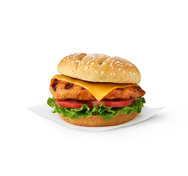 The Grilled spicy Deluxe Sandwich topped with cheese on a bed of lettuce and tomato and sitting on a white napkin