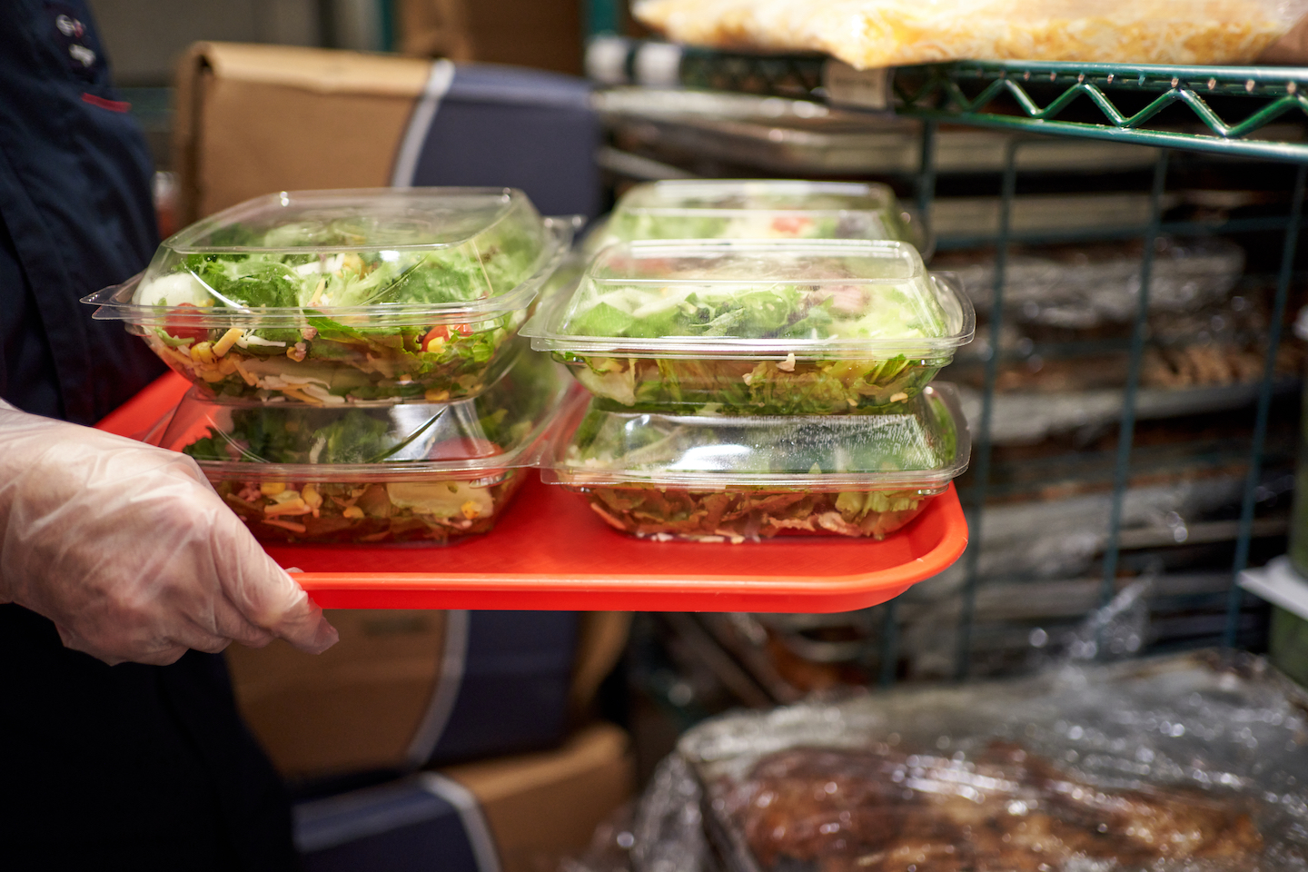 Person carrying a red tray of salads in containers