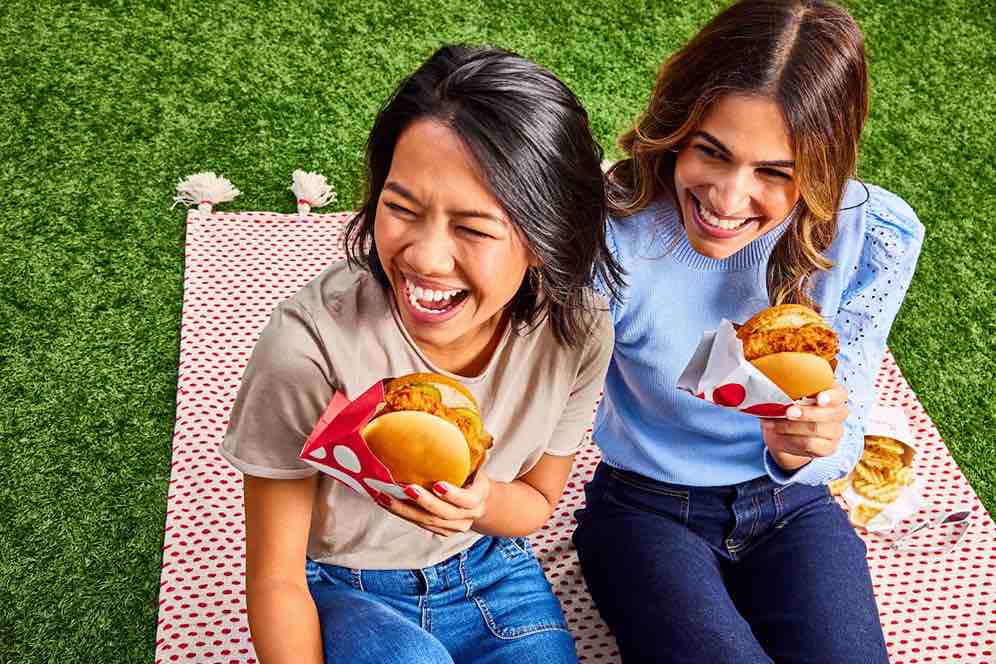 Friends having a picnic and enjoying a Chick-fil-A® Chicken Sandwich, Spicy Chicken Sandwich and Chick-fil-A Waffle Potato Fries®.