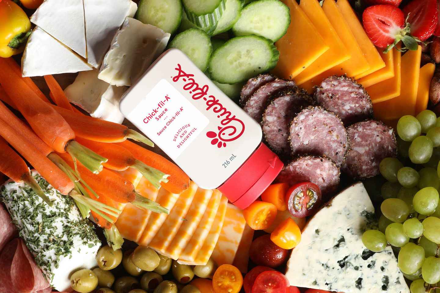 A bottle of 8 oz Chick-fil-A Sauce® on a charcuterie board with fruits, vegetables, cheeses and meats    