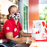 Team member wearing a cow-spots mask looks at the camera as she passes the customer their food tray while wearing gloves
