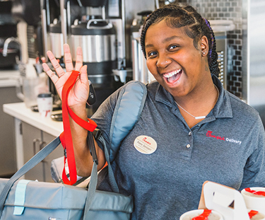 Chick-fil-A® Team Member waving and smiling, holding a delivery bag