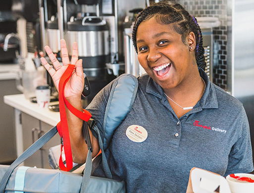 Chick-fil-A® Team Member waving and smiling, holding a delivery bag