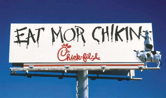 A billboard with the Chick-fil-A Cows on it painting the words “Eat Mor Chikin”