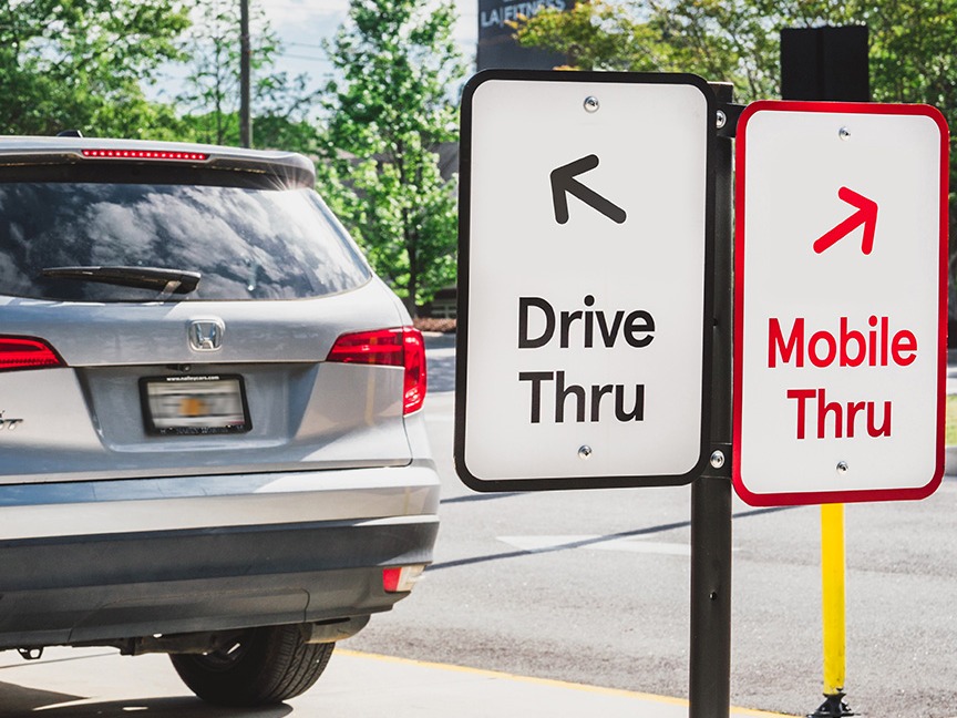 A car in front of two signs: one directing towards the drive thru lane and one directing towards the Mobile Thru lane. 