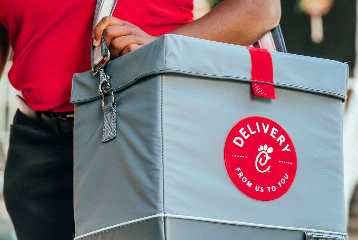 A Chick-fil-A Team Member holds a gray delivery bag that reads, “Delivery: From us to you.” 