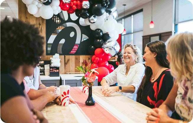 A group of smiling people sitting around a table inside a Chick-fil-A® Restaurant