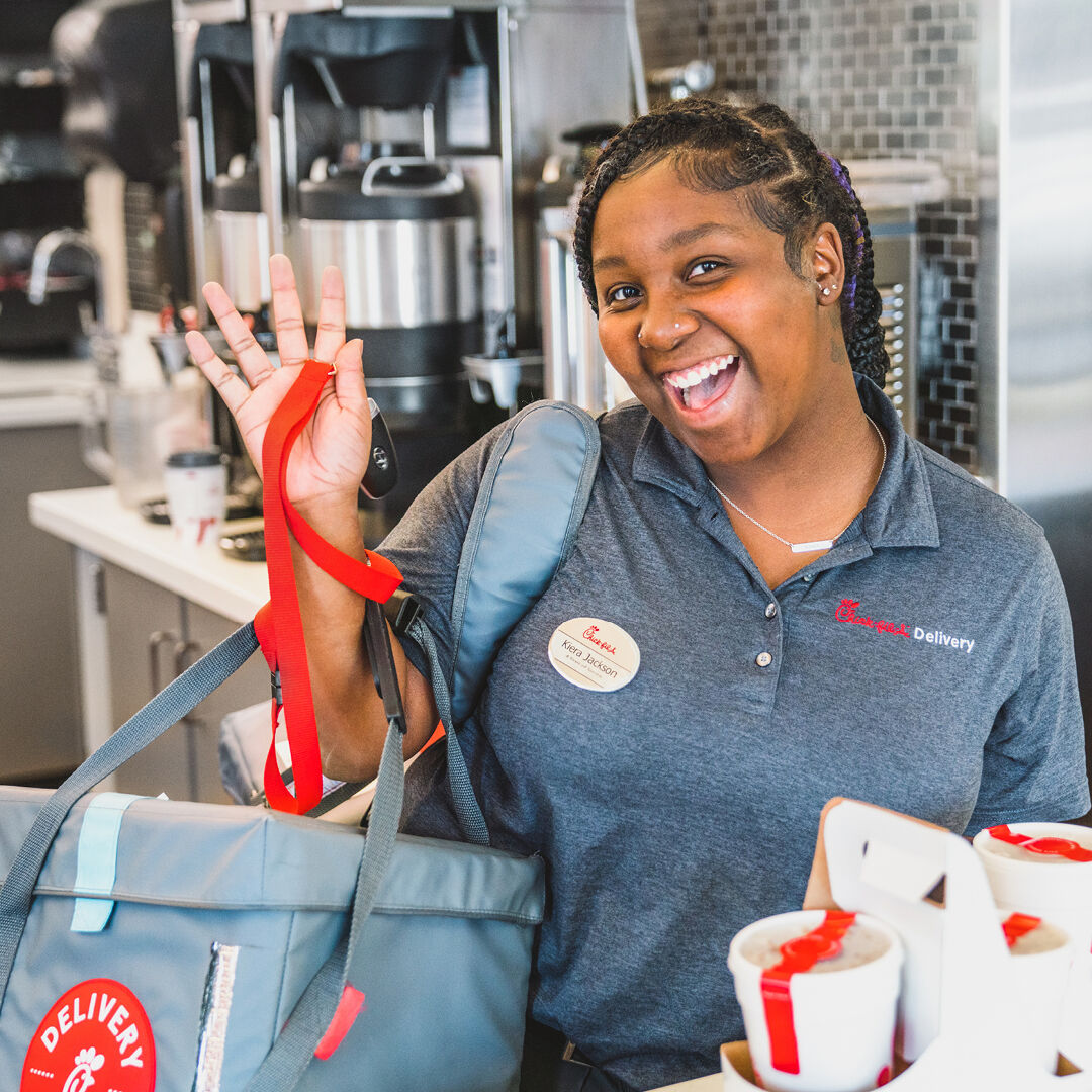 A Chick-fil-A, Inc. employee handing a Team Member a large sauce packet with balloons and confetti around them